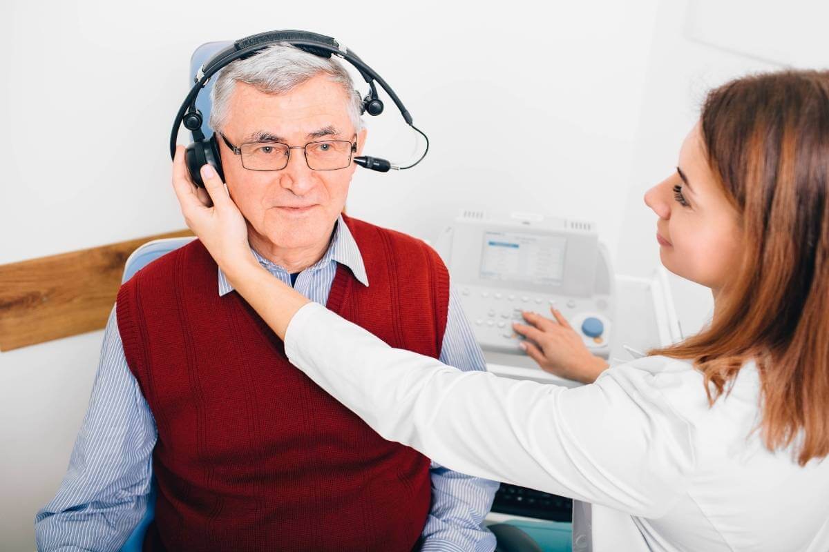 senior man in red vest getting an audiologist exam