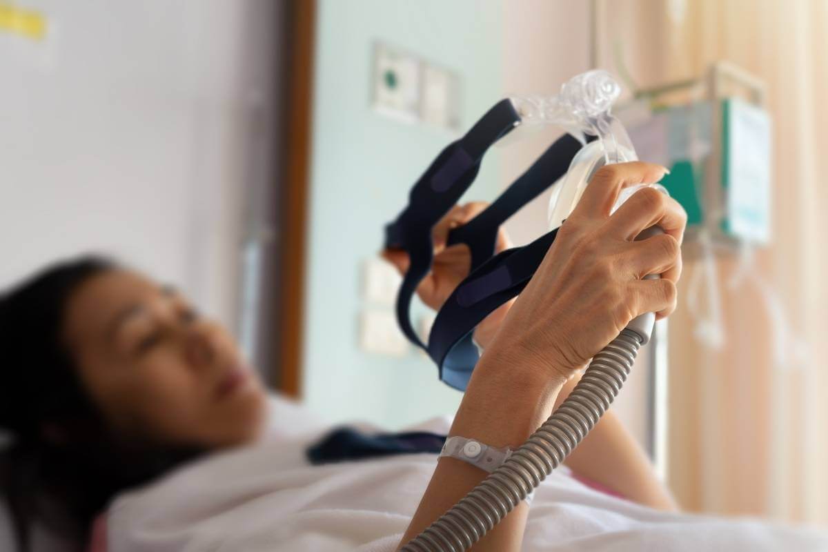 woman in a hospital bed holding a cpap machine