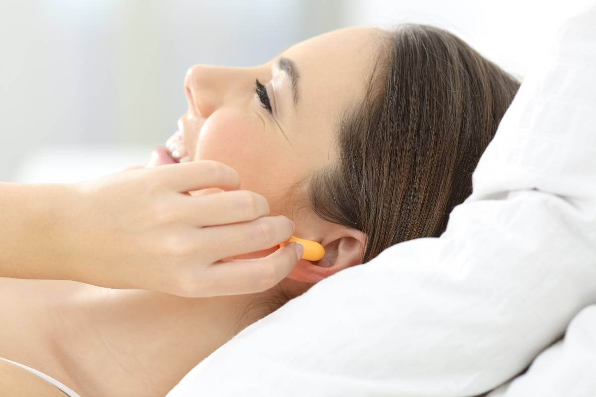 woman lying in bed and putting ear plugs into her ear