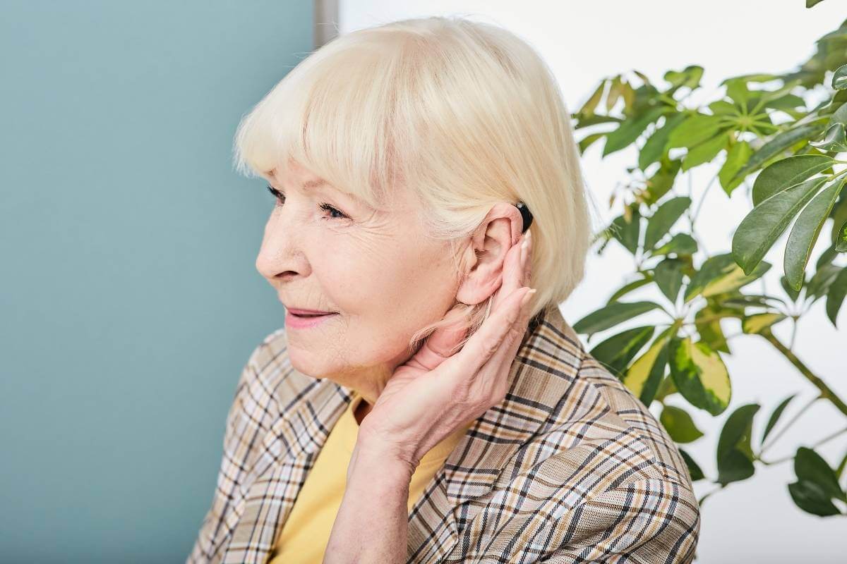 old woman with white hair trying on a hearing aid