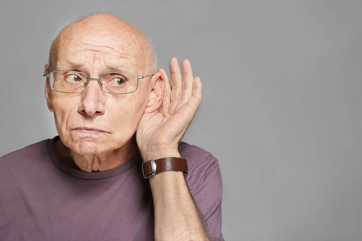 senior man with eyeglasses holding his ear to hear better