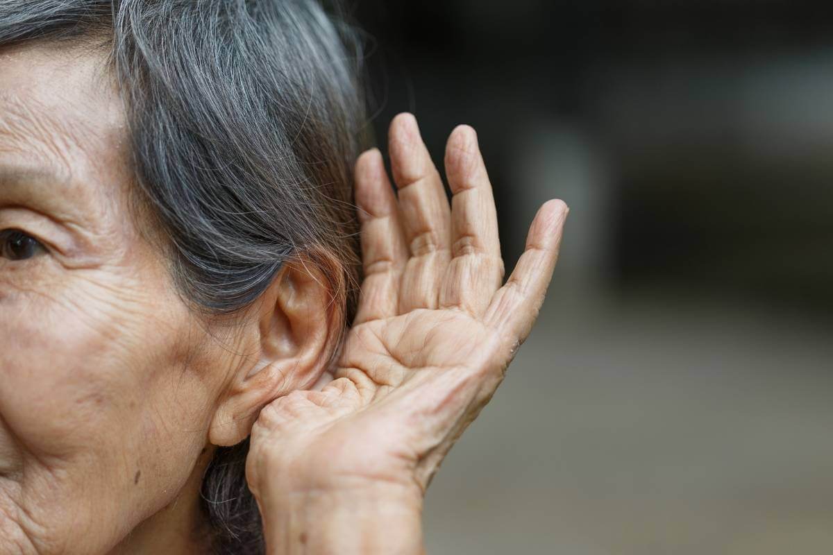 older woman with grey hear using her hand to hear better