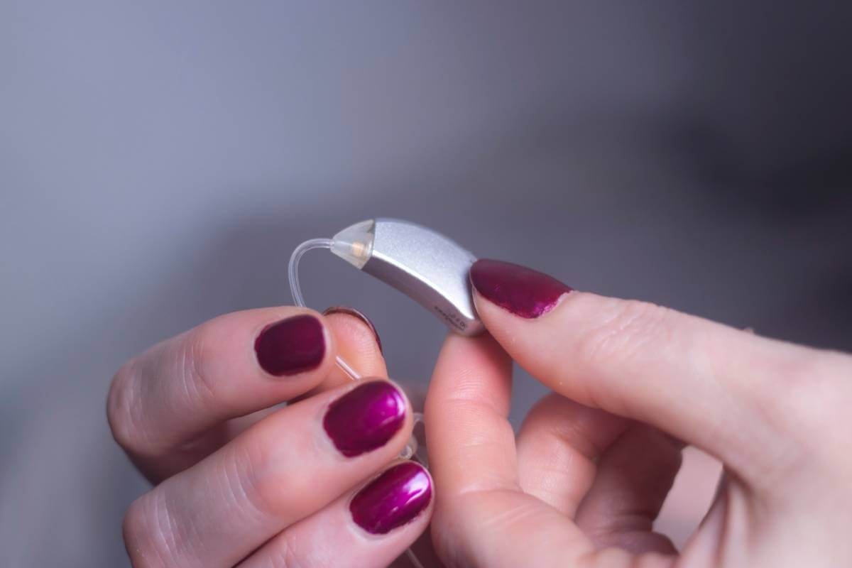 woman with painted nails holding a hearing aid